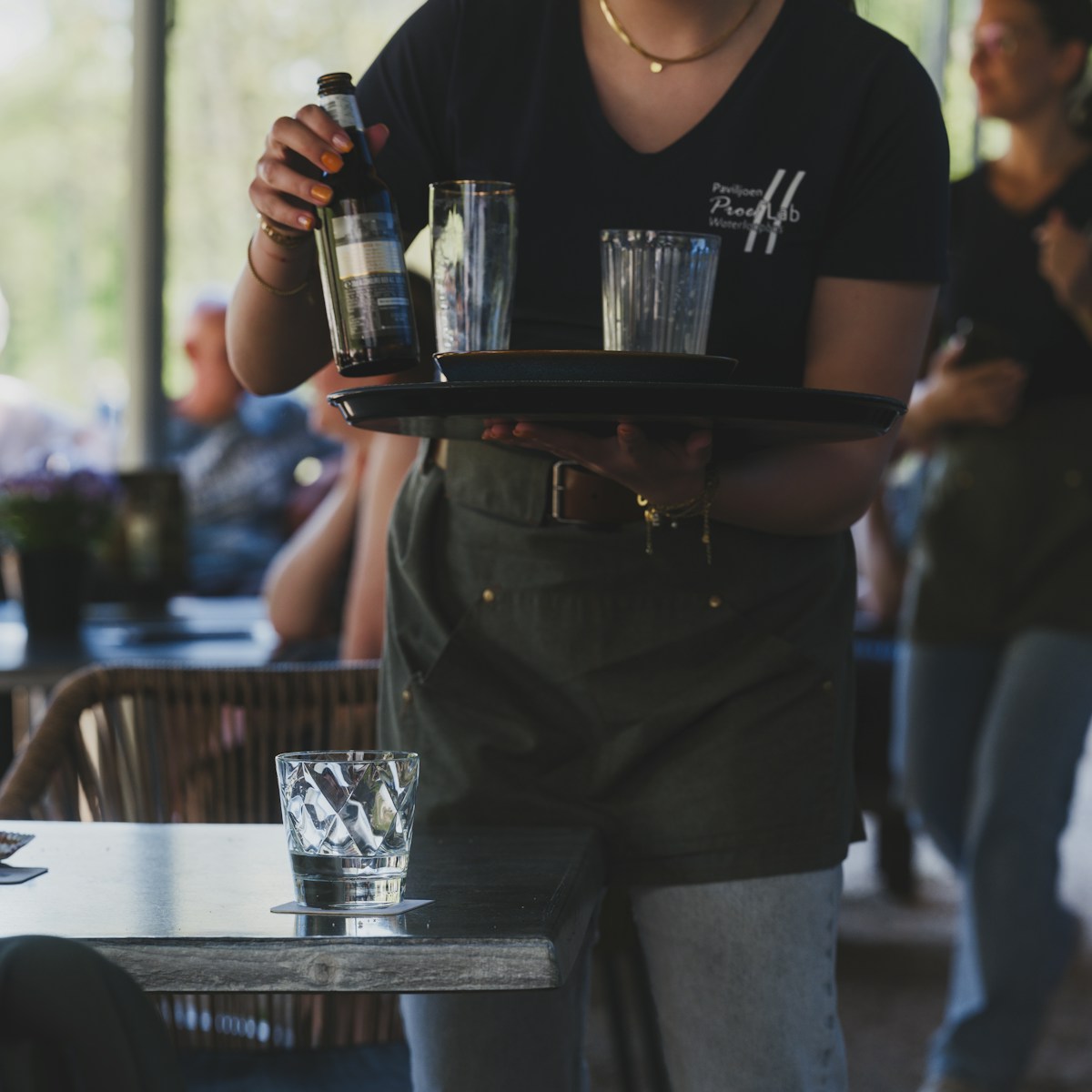 A waitress carries a tray with glasses and a bottle.